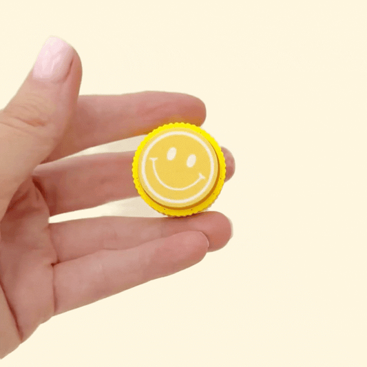round fidget clicker with raised face icon and textured rim
