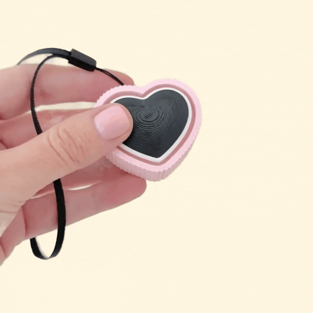 A heart-shaped clicker fidget toy with a pink ridged outer section and a black centre.