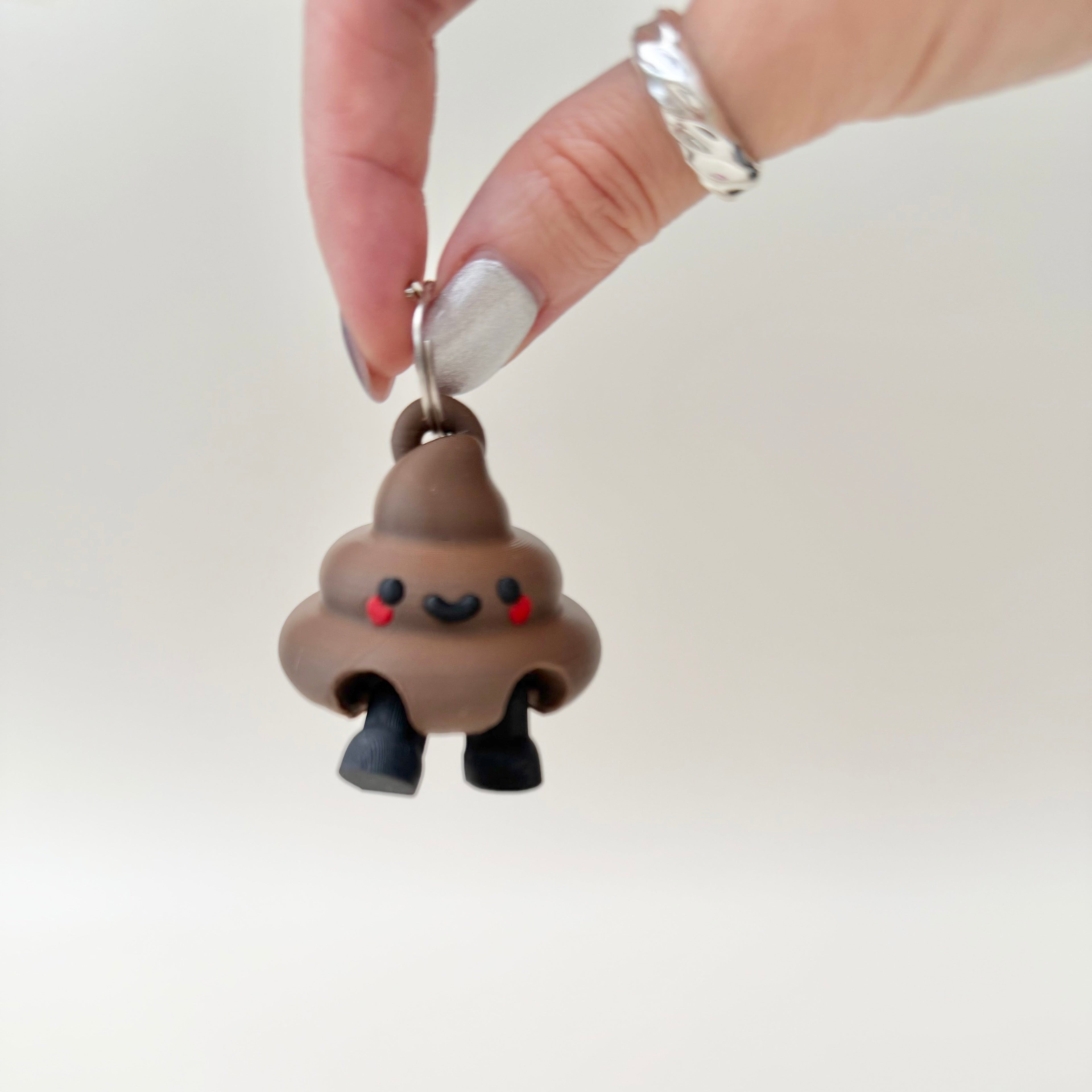 Poop-themed lanyard accessory with a cute face and dangling legs that can also sit on a shelf or desk.
