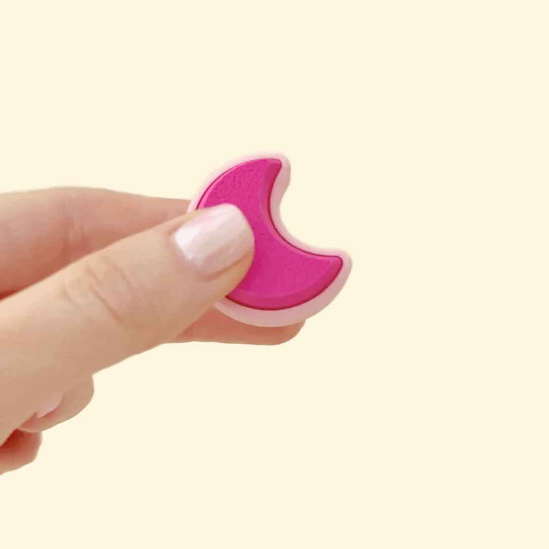 Handheld moon-shaped clicker fidget toy in pastel pink tones for sensory play.