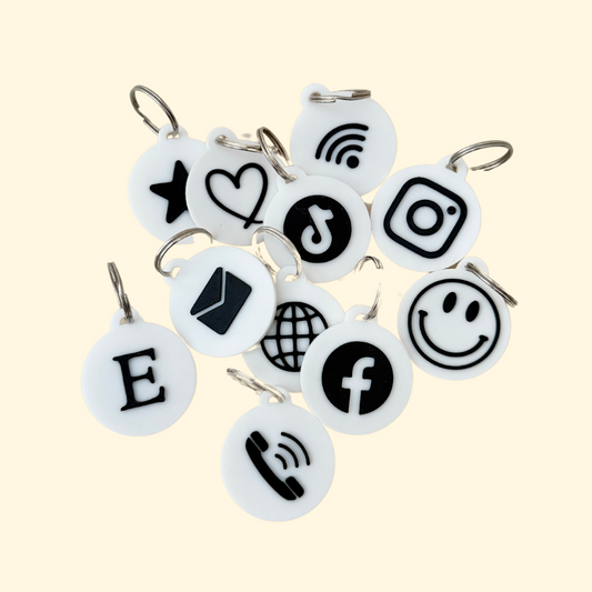 A close-up of NFC keyrings in black and white, featuring various icons like a heart, phone, and Wi-Fi symbol, highlighting their versatility for programming and use.