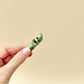 Side profile of a green metallic pickle fidget toy with textured ridges and a bitten chunk.
