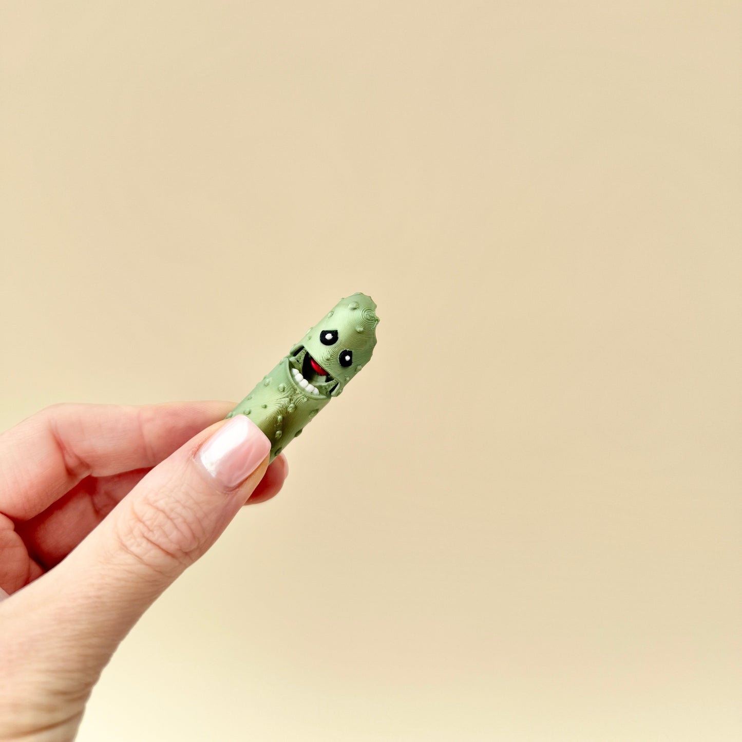 Side profile of a green metallic pickle fidget toy with textured ridges and a bitten chunk.