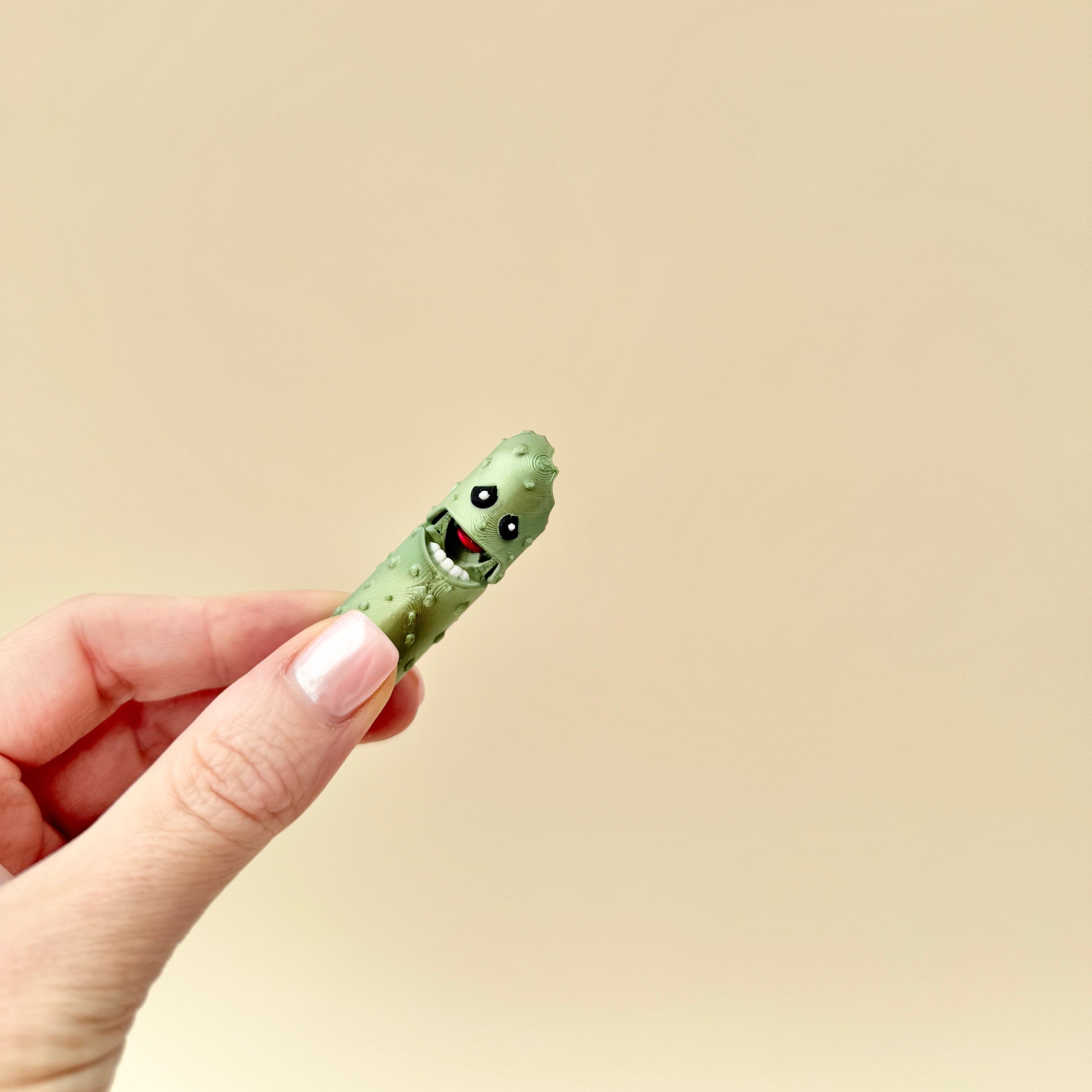 Side profile of a green metallic pickle fidget toy with textured ridges and a bitten chunk.