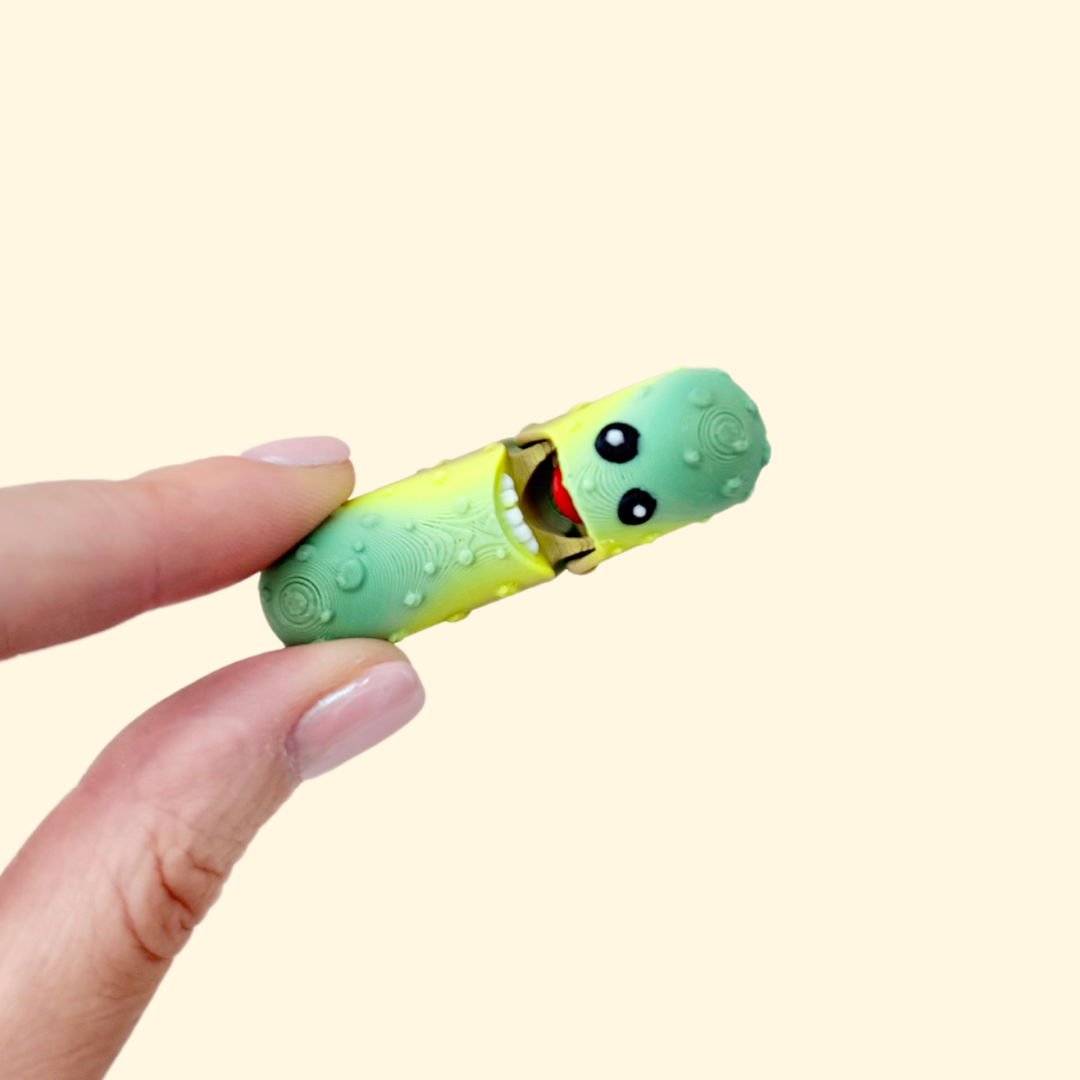 A green gradient pickle fidget toy with textured bumps, black and white eyes, and an interactive mouth that reveals teeth and tongue.
