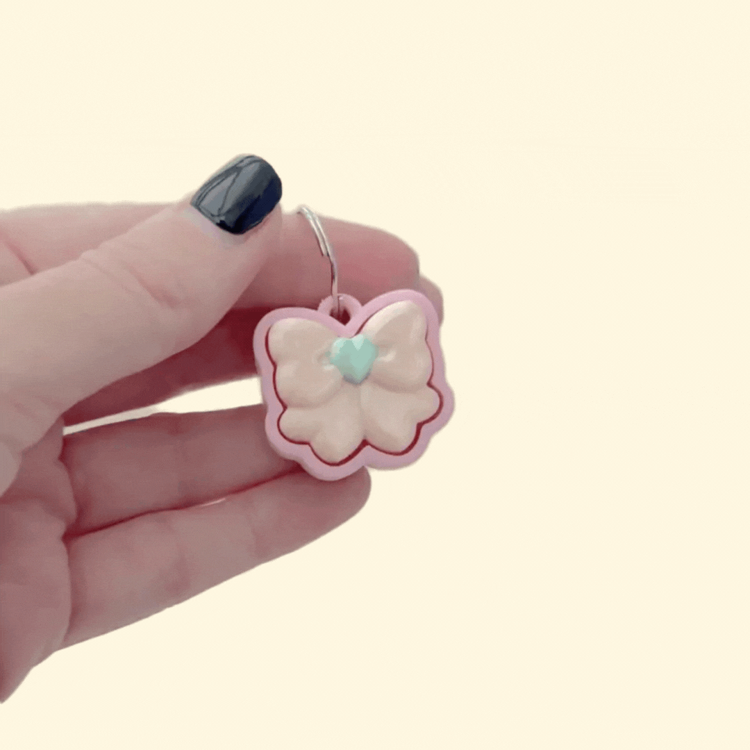 mini bow-shaped clicker with smooth top and metal loop for attaching to keys or bags
