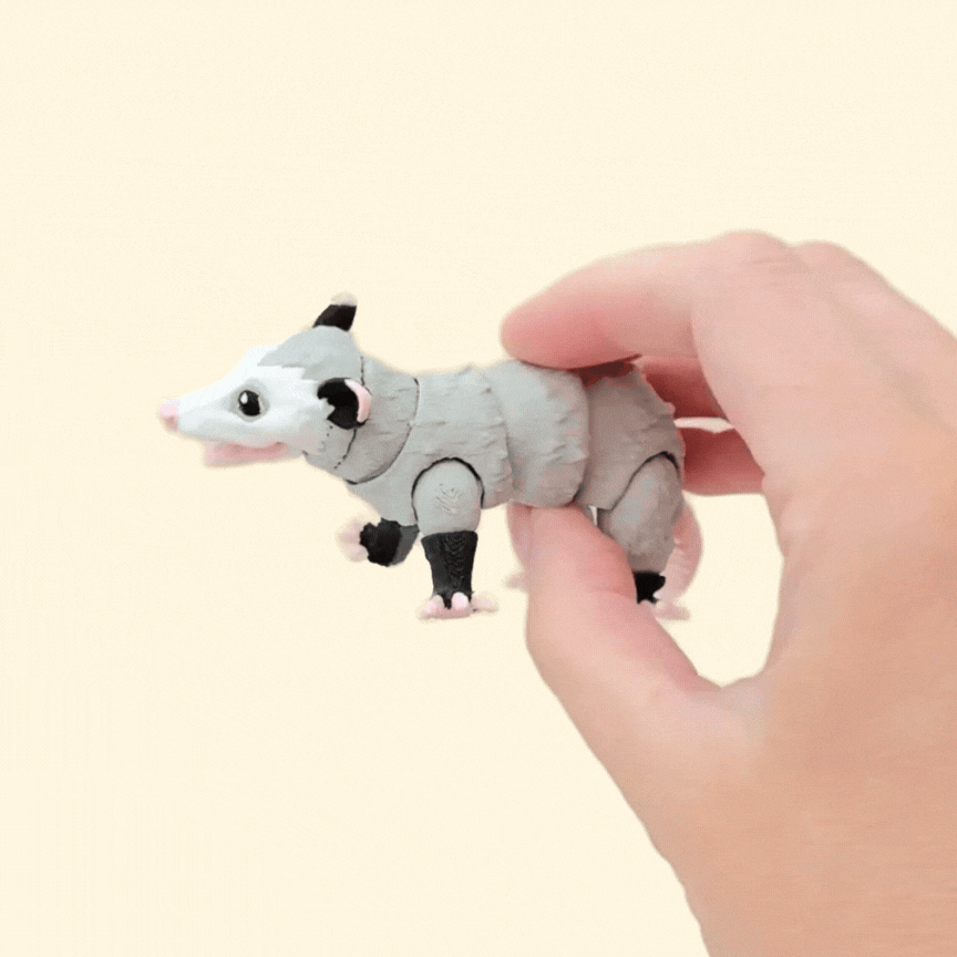 A fully flexible, realistic possum fidget toy with a textured fur-like surface in grey, black, and white. Features a poseable tail, movable legs, and an articulated mouth.