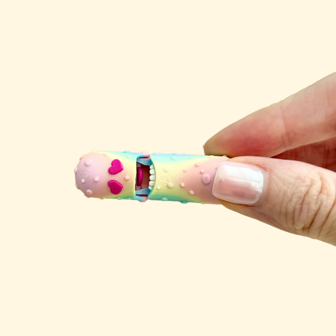 A rainbow-coloured pickle-shaped fidget toy with heart-shaped red eyes, perfect for sensory play.