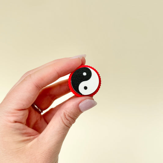 Pocket-sized clicker with smooth tactile movement and symbolic design.