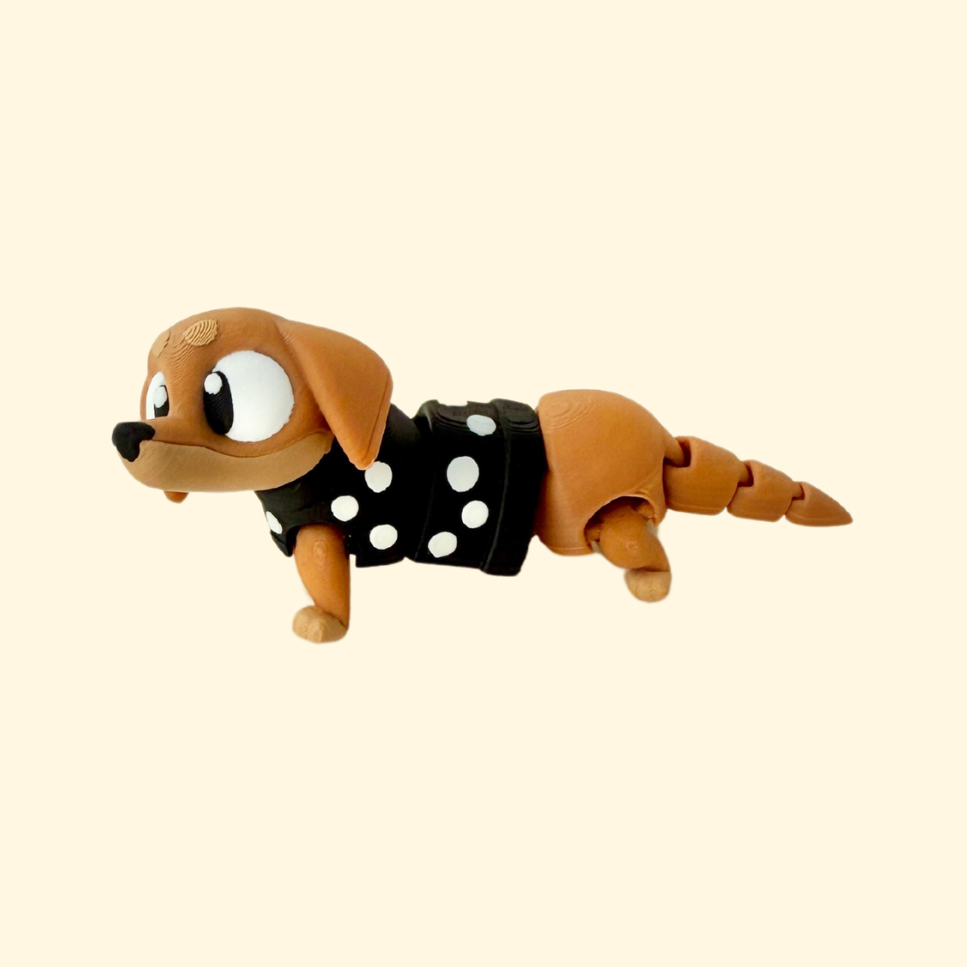 A flexible sausage dog fidget toy with a wiggly body, movable head and tail, brown and beige design, black nose, and a spotty black and white jumper.