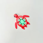 A red fidget toy shaped like a turtle with a strawberry-themed shell featuring white spots and a green pattern.