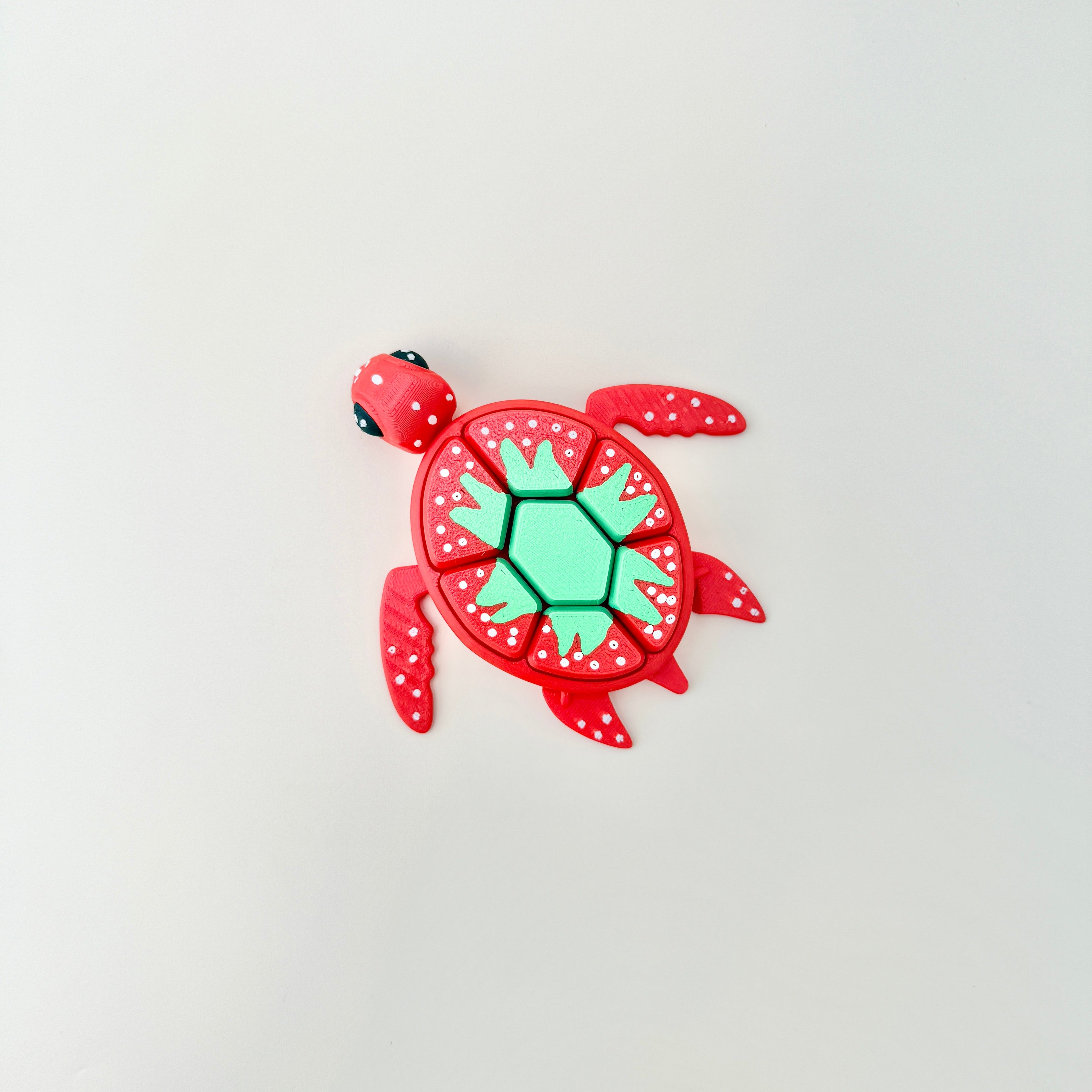 A red fidget toy shaped like a turtle with a strawberry-themed shell featuring white spots and a green pattern.