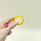 Yellow sensory clicker designed as a fun school reward or desk toy.