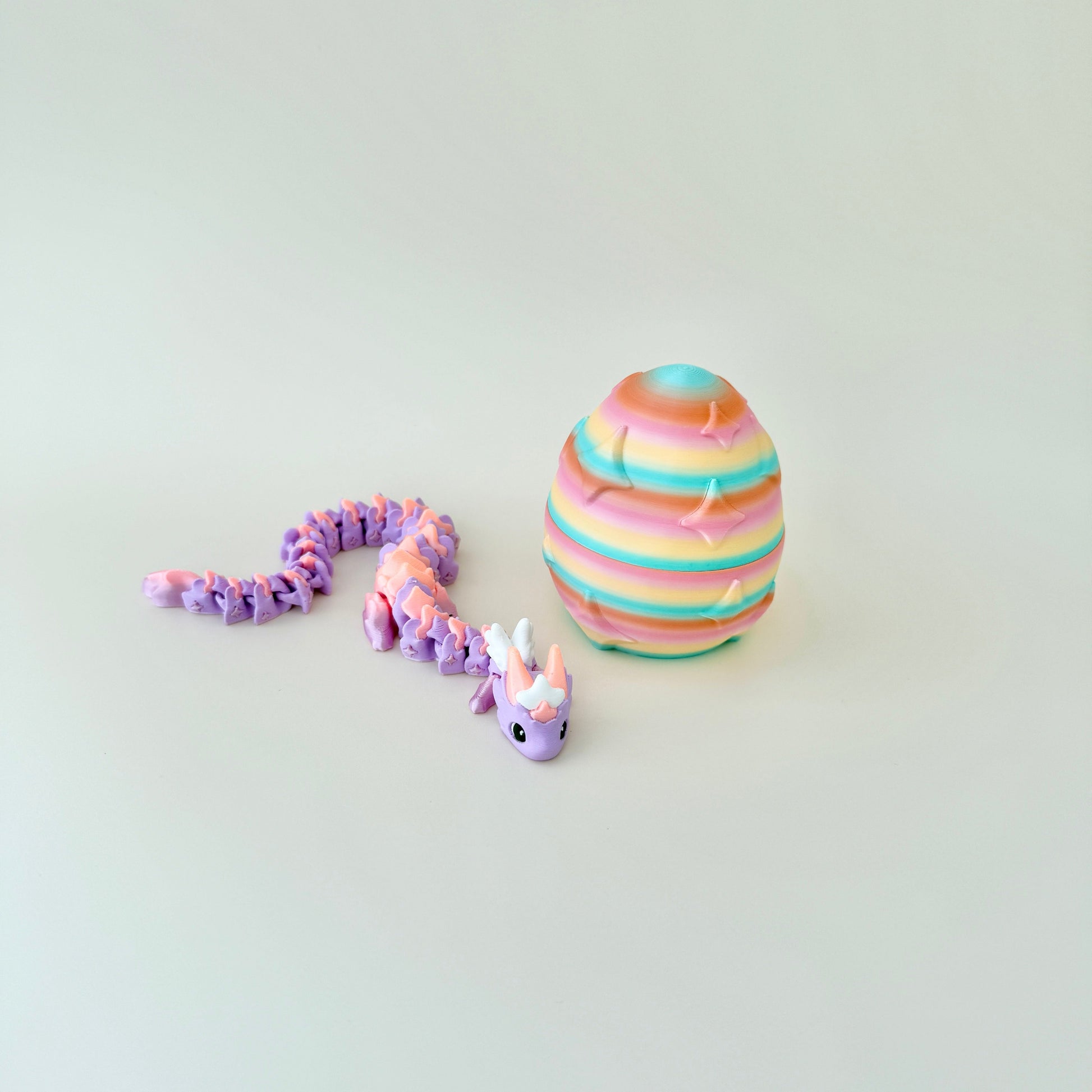 Gradient lilac and peach dragon resting beside a rainbow egg embossed with twinkling stars.