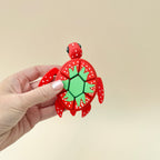A sensory fidget toy designed as a large red turtle with a green strawberry-inspired shell and black beady eyes.