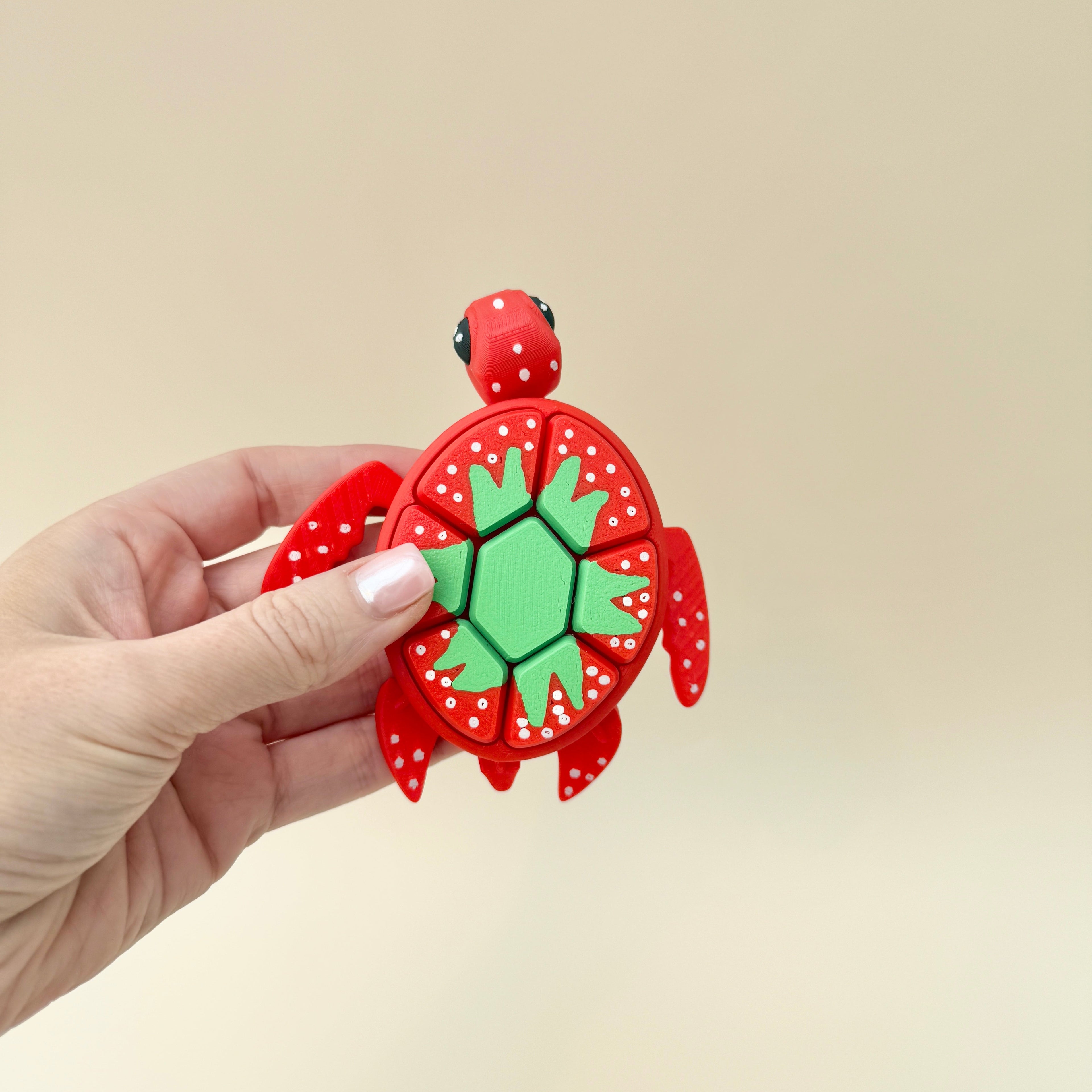 A sensory fidget toy designed as a large red turtle with a green strawberry-inspired shell and black beady eyes.
