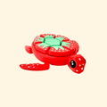 A bright red turtle-shaped fidget clicker with white seed spots, a green leaf design on its back, and black eyes.