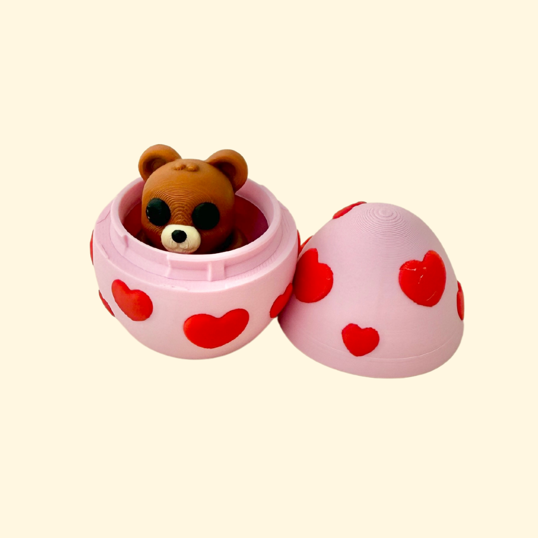 A flexible teddy bear fidget toy that fits inside a pink egg with red hearts, making it a perfect portable sensory toy.