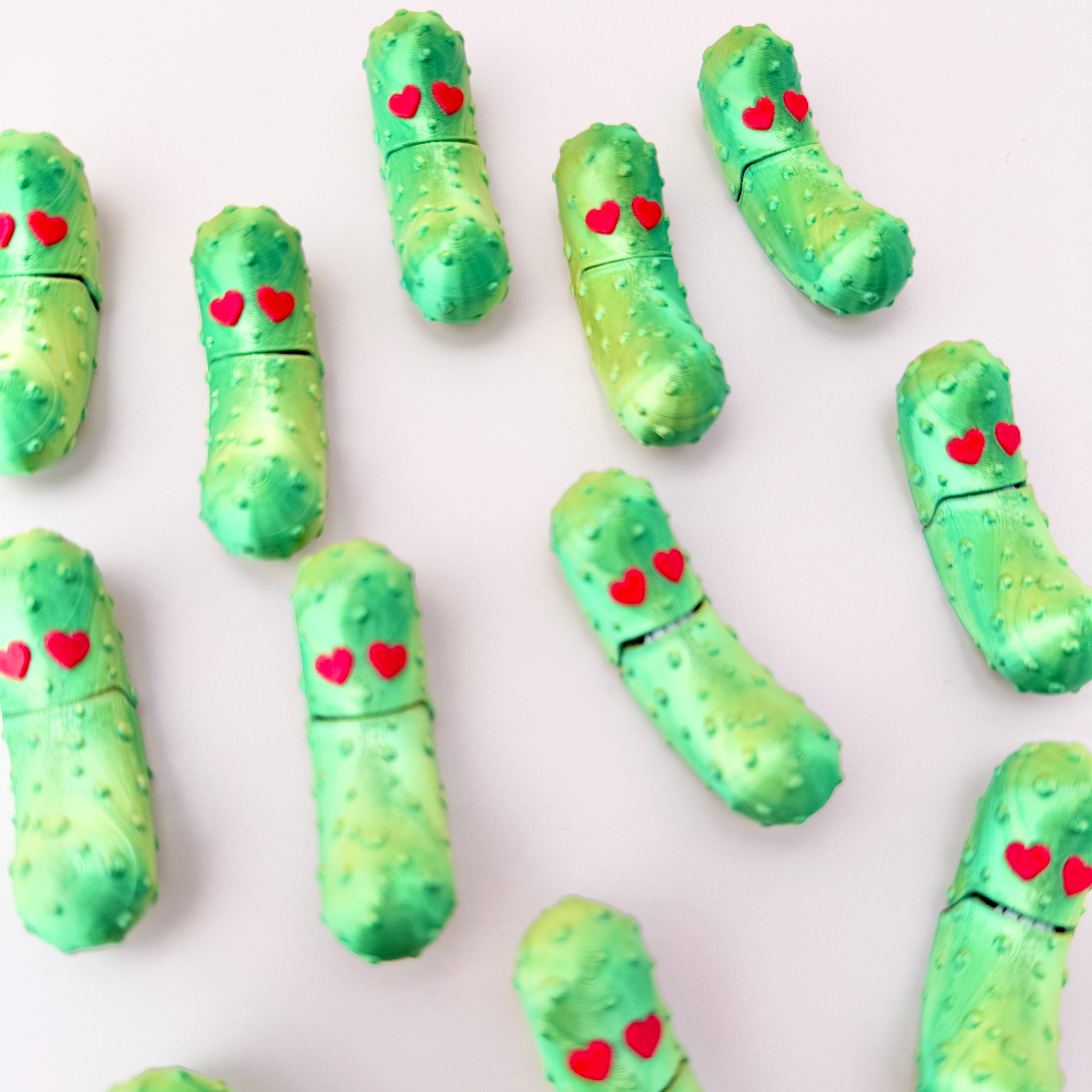 A shiny green pickle toy with gold highlights, heart eyes, and playful sensory features.