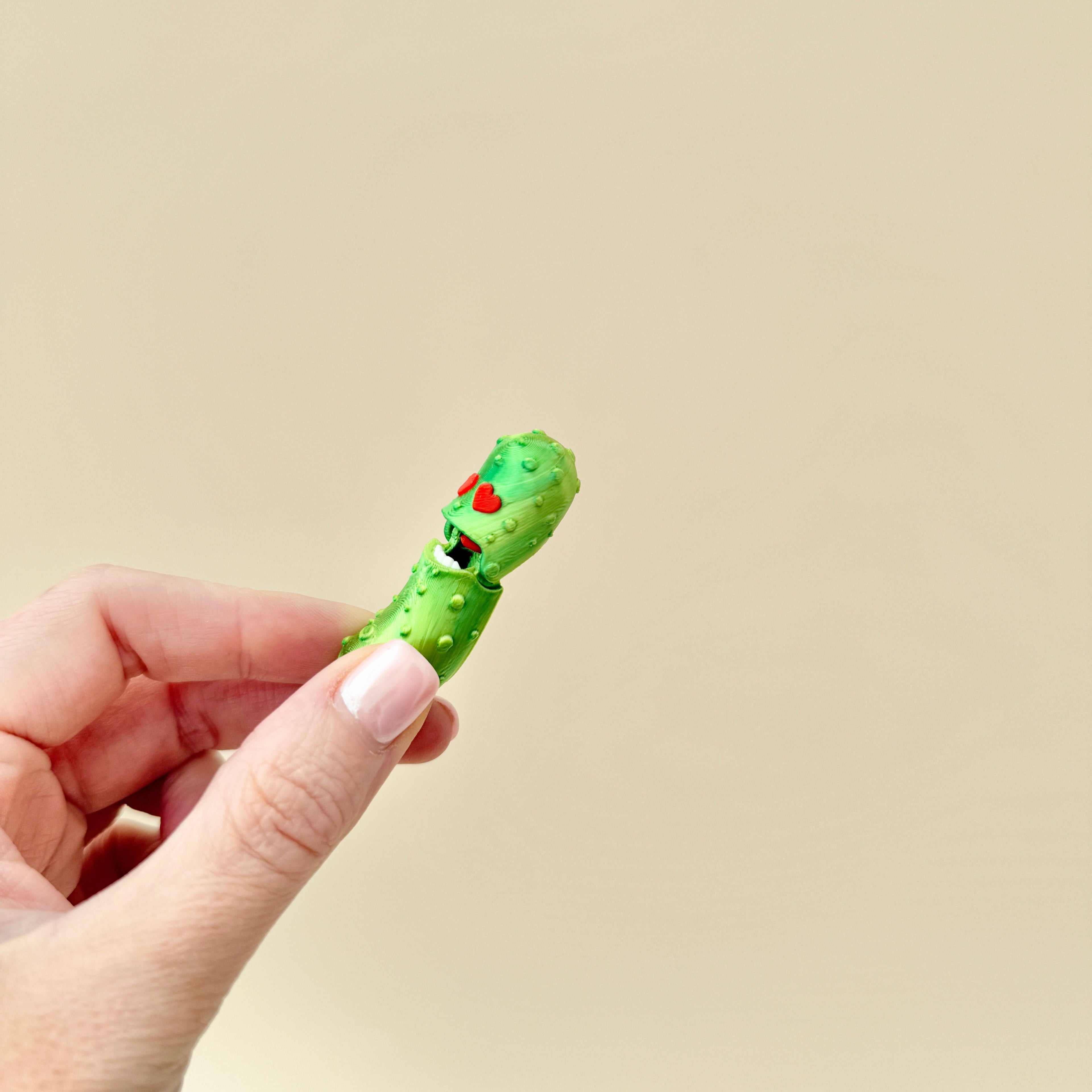 A quirky fidget toy shaped like a pickle, featuring red heart eyes and textured details.