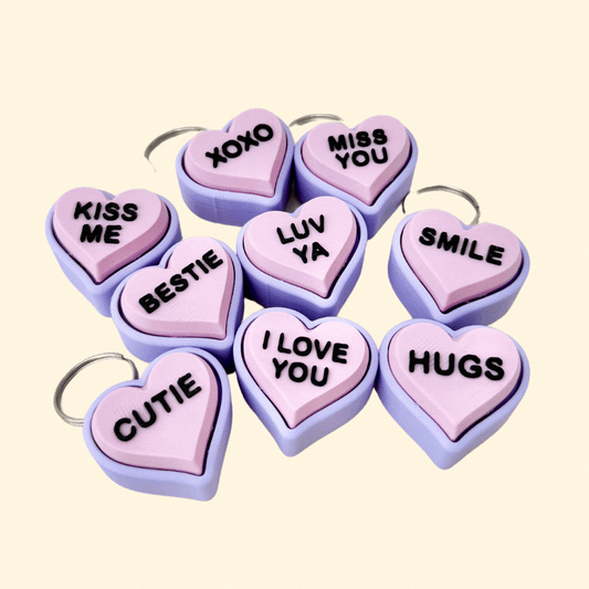 A lilac and pink heart-shaped fidget clicker keyring with heartfelt messages, designed as a portable Valentine’s Day gift.