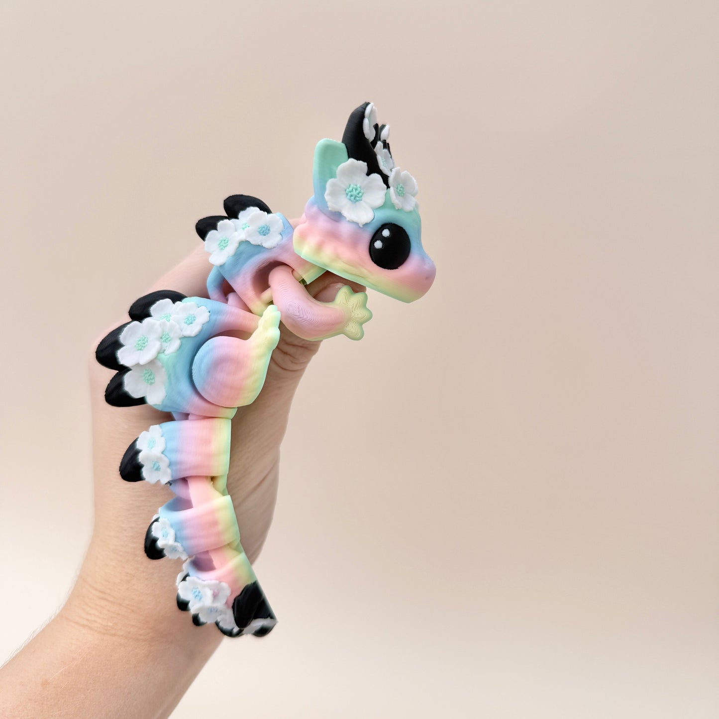 Articulated dragon toy featuring soft rainbow hues, white flowers, and black horns.