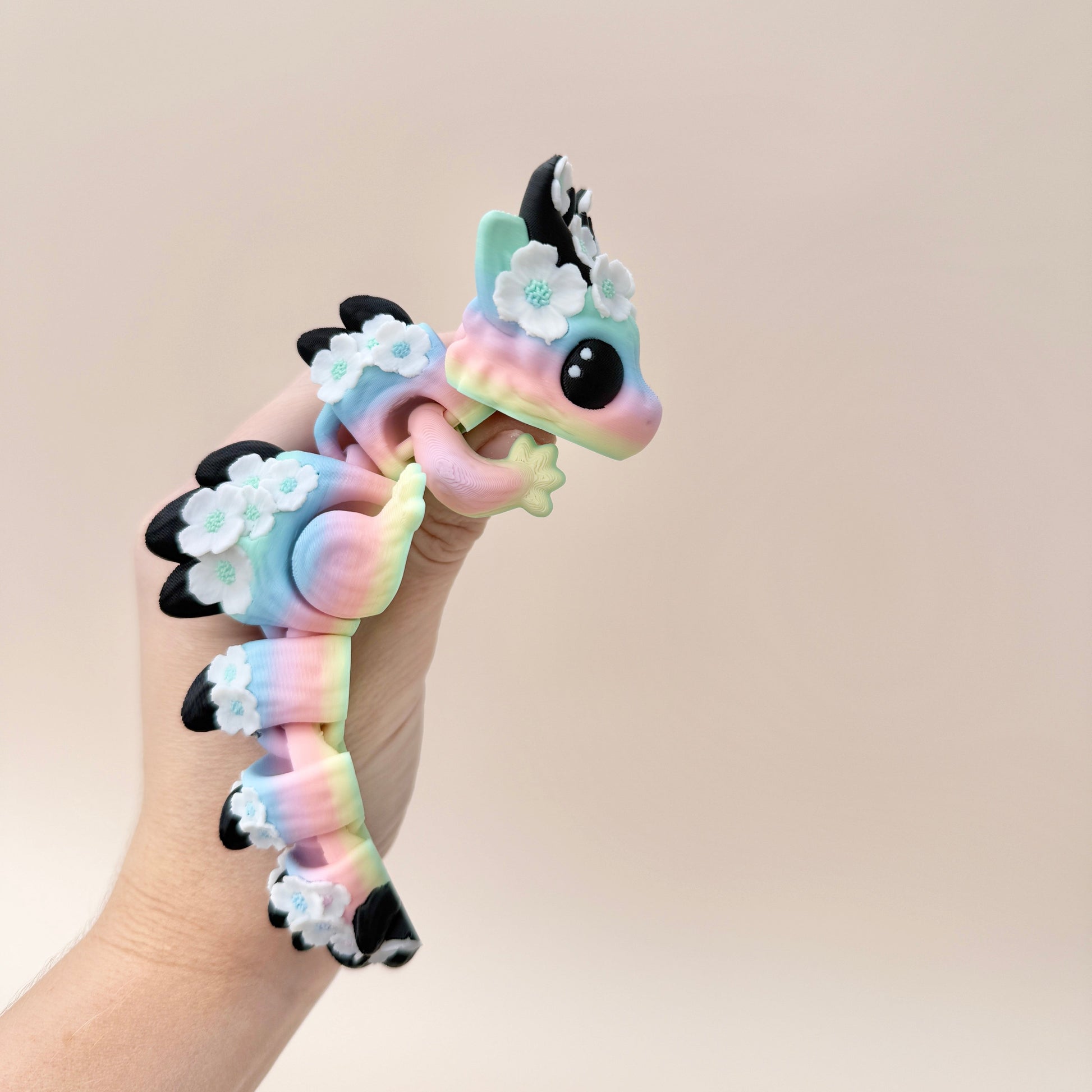 Articulated dragon toy featuring soft rainbow hues, white flowers, and black horns.