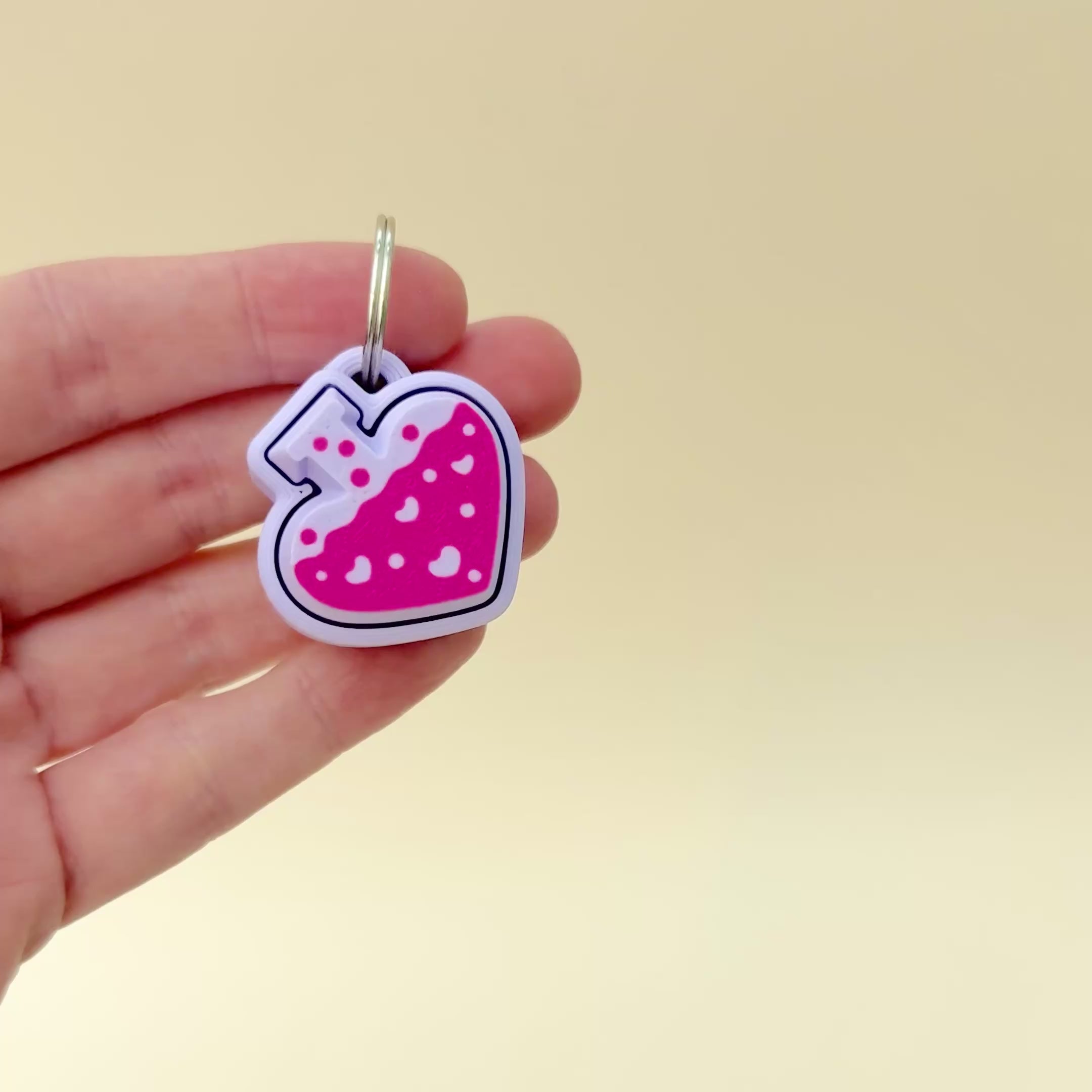 A 4cm lilac potion bottle-shaped keyring fidget toy with bright pink liquid and heart details.