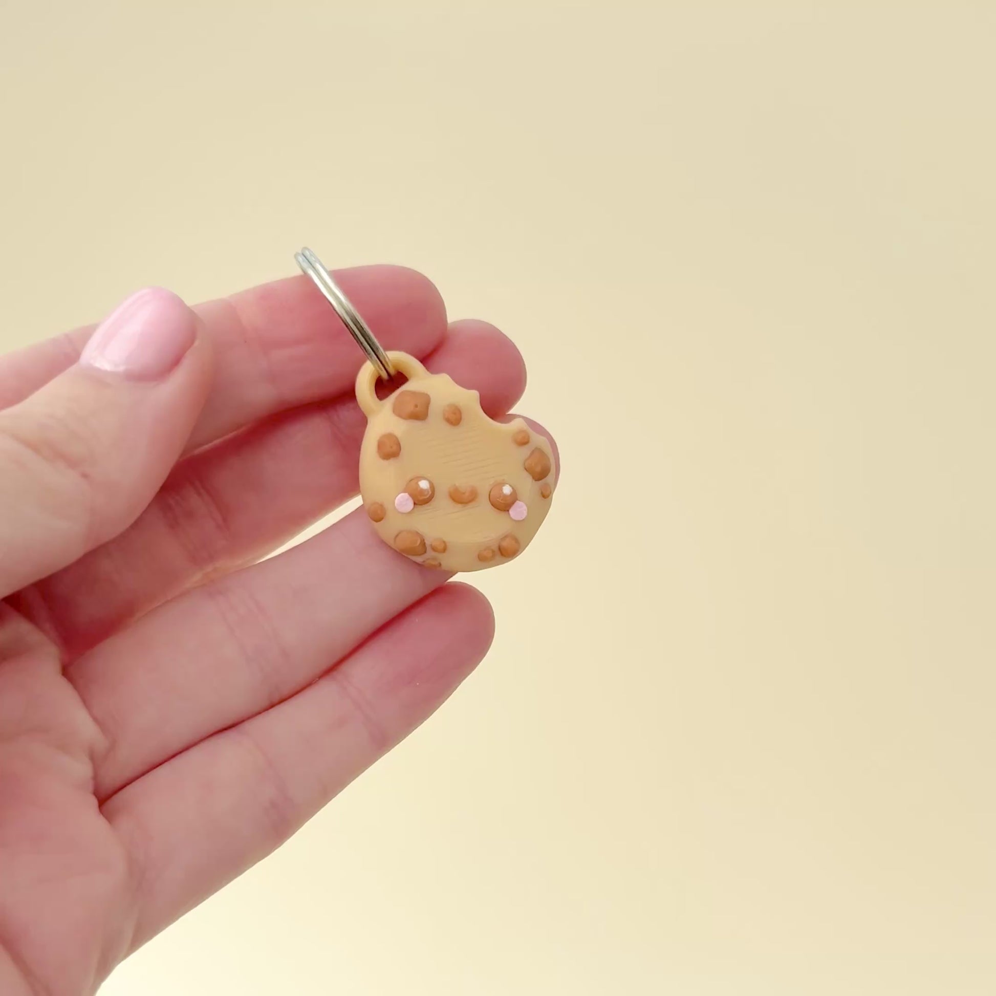A mini cookie charm keyring with pink cheeks and a bite detail, perfect for gifts.
