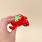 A red turtle clicker fidget toy with a green and white strawberry-style design on its shell, featuring 7 clickable spots.
