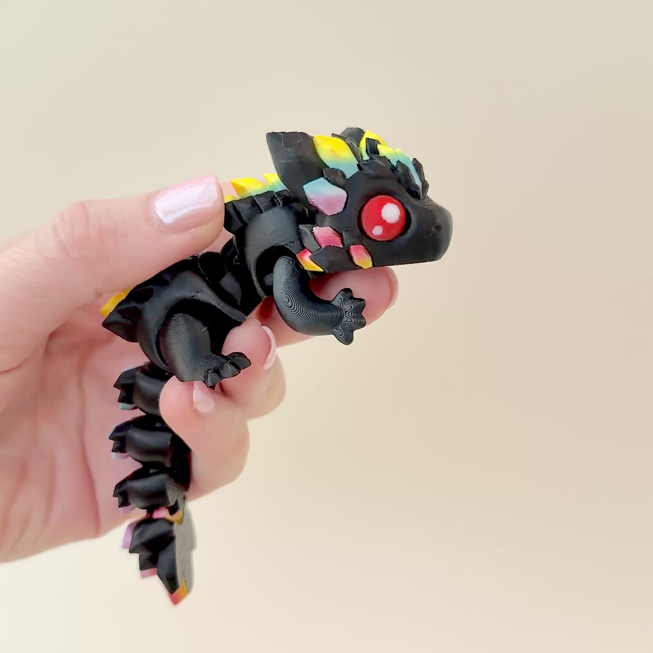 Black dragon fidget toy featuring rainbow gem-like features, articulated body, and bold red eyes.