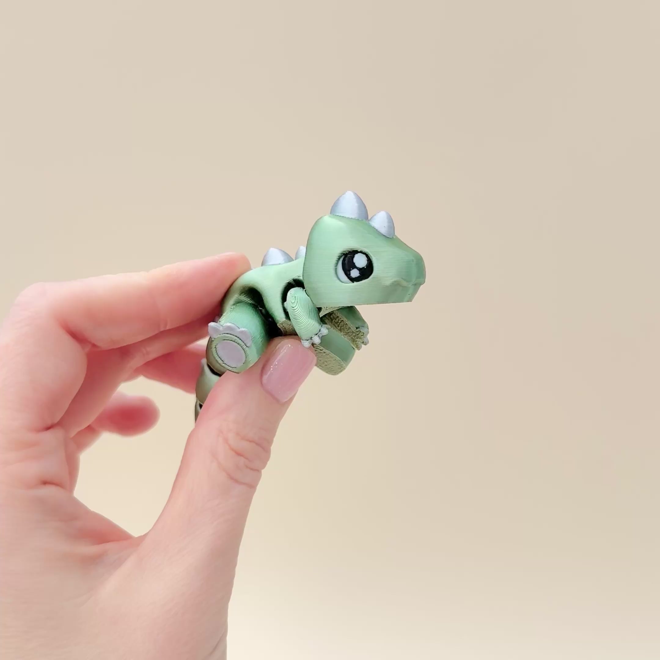 Compact dinosaur fidget toy featuring detailed claws, spikes, and articulated design in two colours.